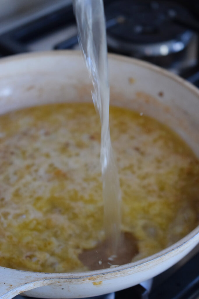 Adding chicken broth to a skillet.