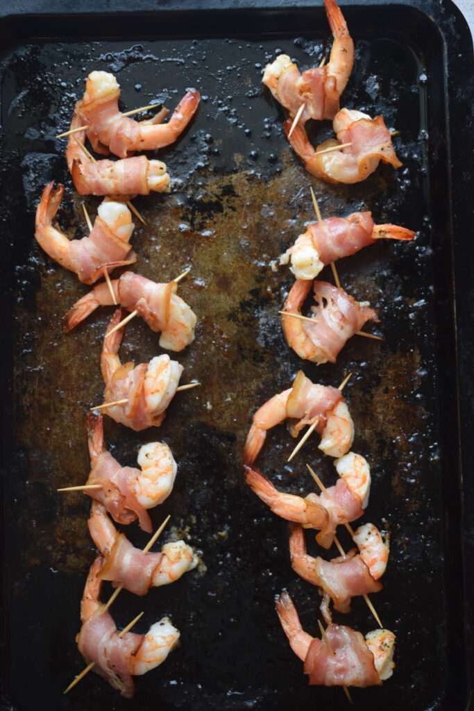 Cooked shrimp wrapped in bacon on a baking tray.