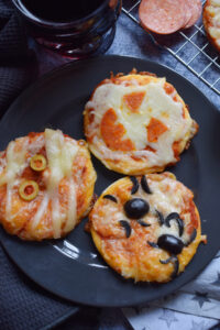 Three Halloween pizzas on a black plate.