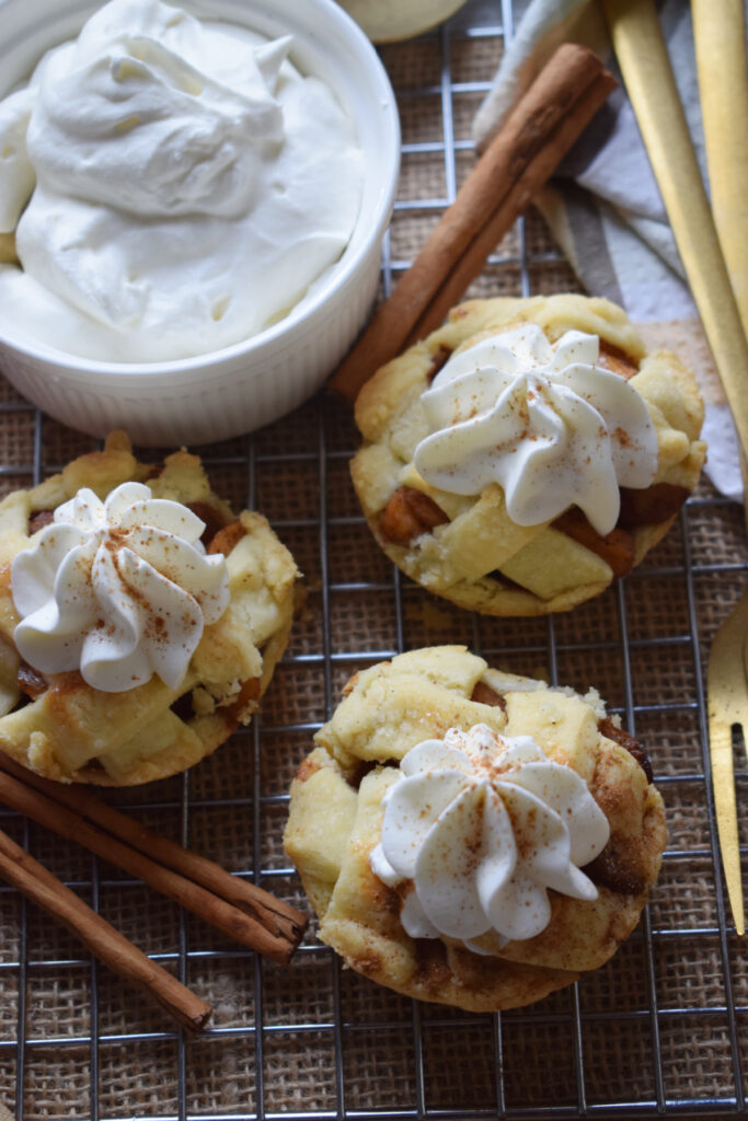 Whipped cream topped mini apple pies with a bowl of whipped cream.