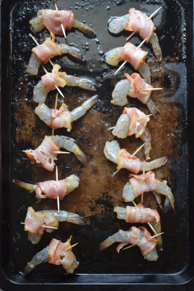 Shrimp wrapped in bacon on a baking tray.