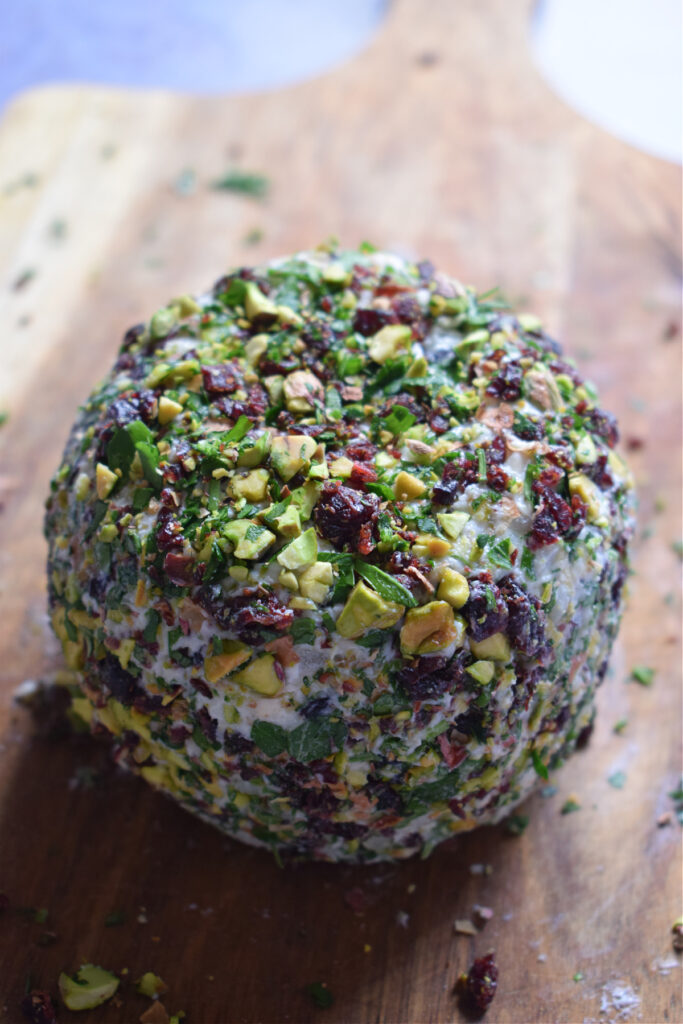 Cranberry and Pistachio Goat cheese ball on a wooden board.