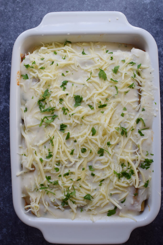 Cannelloni topped with bechamel sauce in a baking tray.
