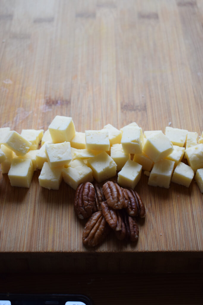 Pecan nuts and cubed cheddar cheese on a wooden board.