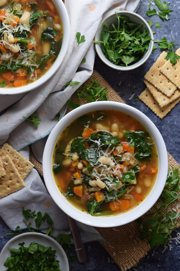 Two bowls of soup with crackers and parsley on the side.