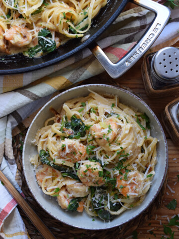 Pasta with shrimp and spinach in a bowl on a table.