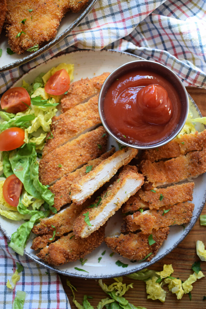 Chicken cutlets cut up on a plate with dipping sauce.