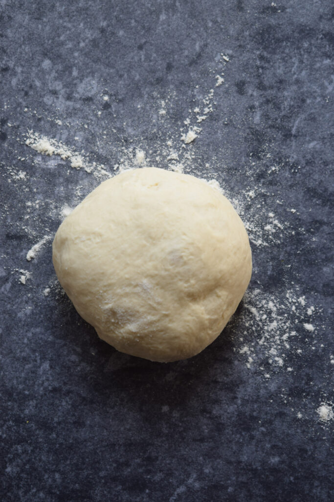 Ball of pizza dough on a dark surface.