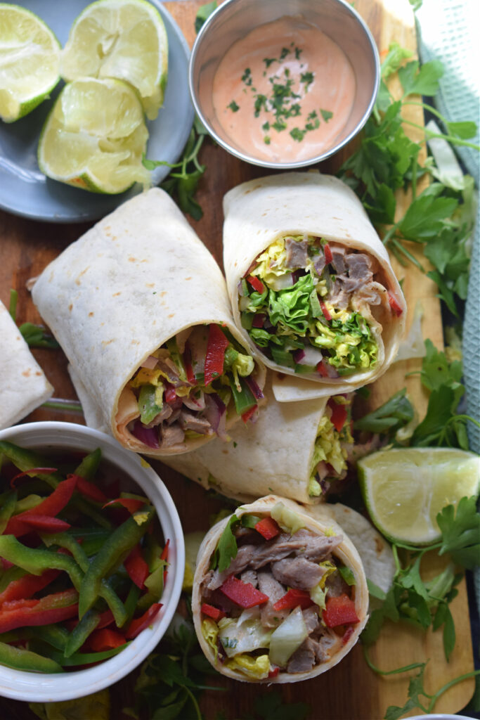 Beef salad wraps on a board with sauce and lime wedges.