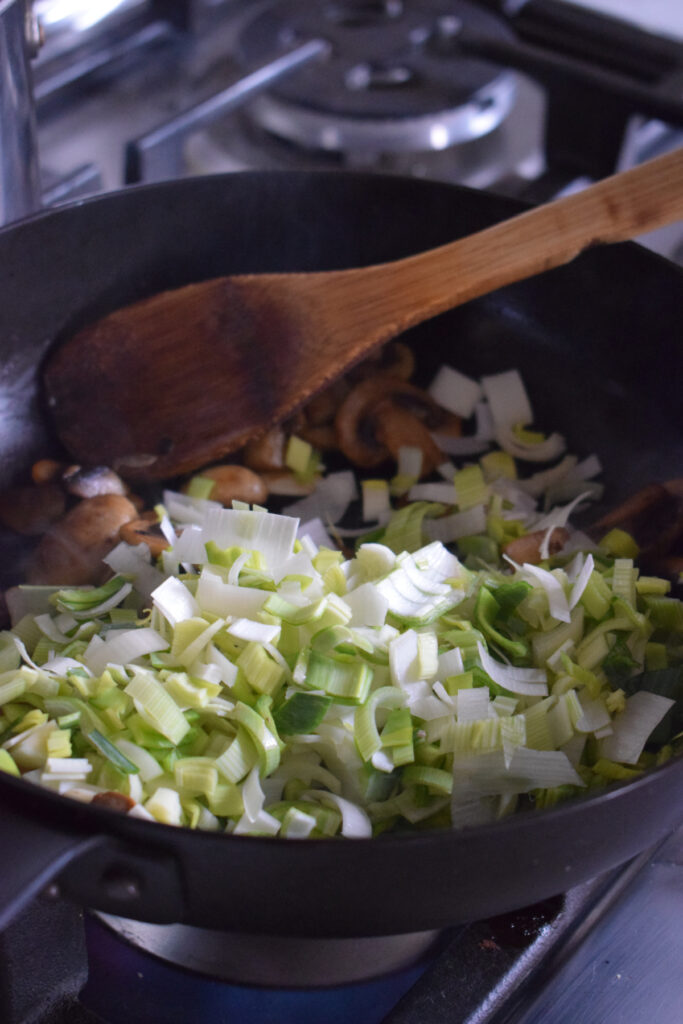 Adding leeks to a skillet and cook down.
