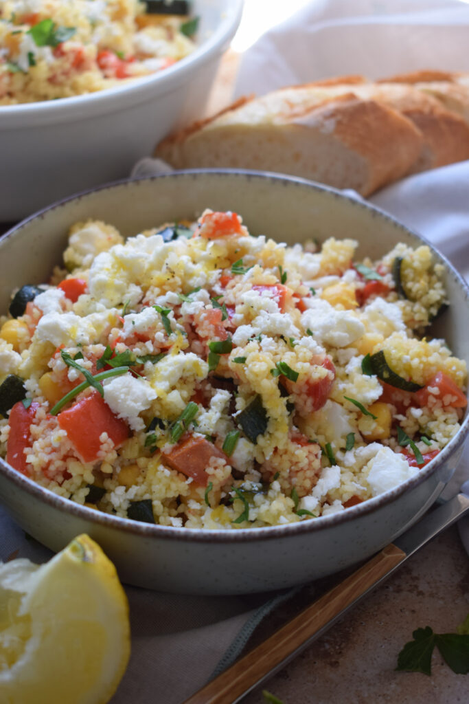 Couscous salad in a bowl with lemon wedges.