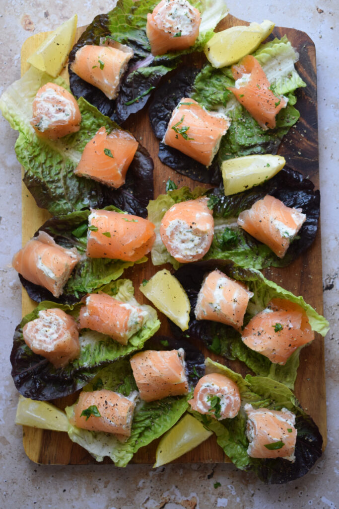 Smoked salmon rolls on a bed of lettuce with lemon wedges.
