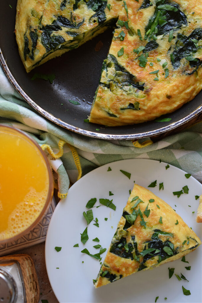 Frittata in a skillet with a glass of juice.