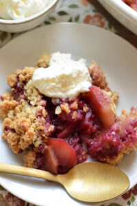 Mixed berry and apple crisp on a plate with whipped cream.