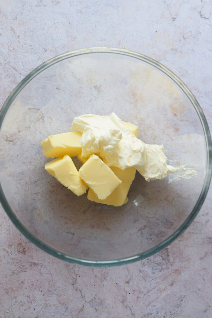 Adding cream cheese with butter in a glass bowl.