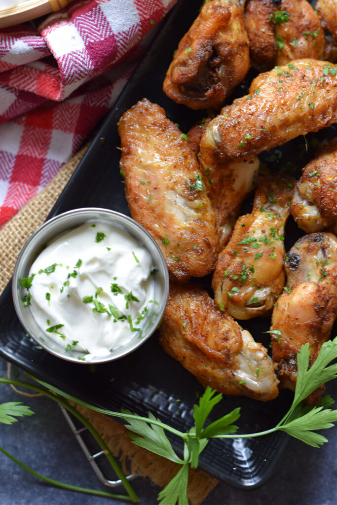 Close up of Old Bay seasoned chicken wings with a sour cream dip.