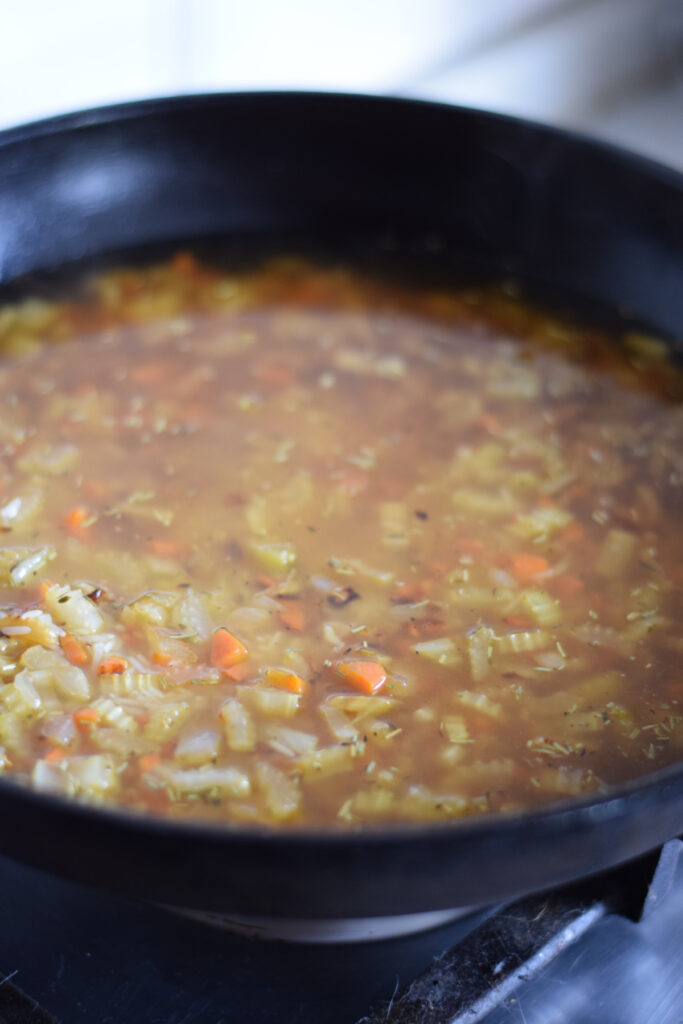 Adding broth to a skillet with rice and vegetables.