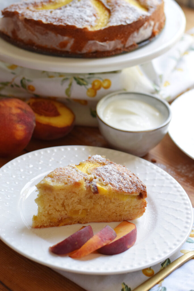 A slice of peach cake on a plate with peach slices.
