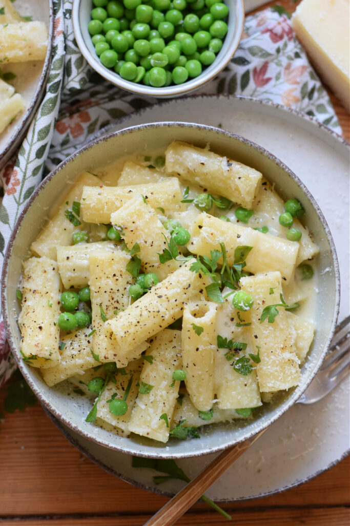 Rigatoni pasta in a bowl with a cream sauce and peas.