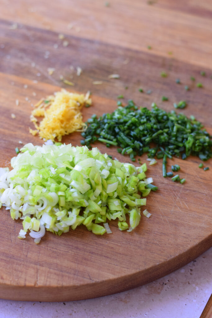 Chopped herbs and lemon zest on a wooden board.