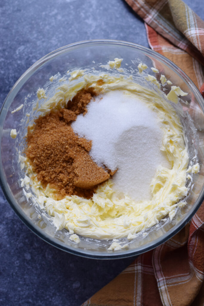 Adding sugar to butter in a glass bowl.