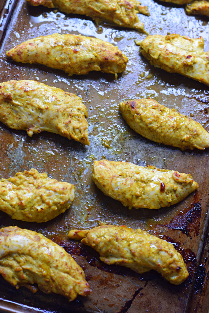Baked tandoori chicken tenders on a baking tray.
