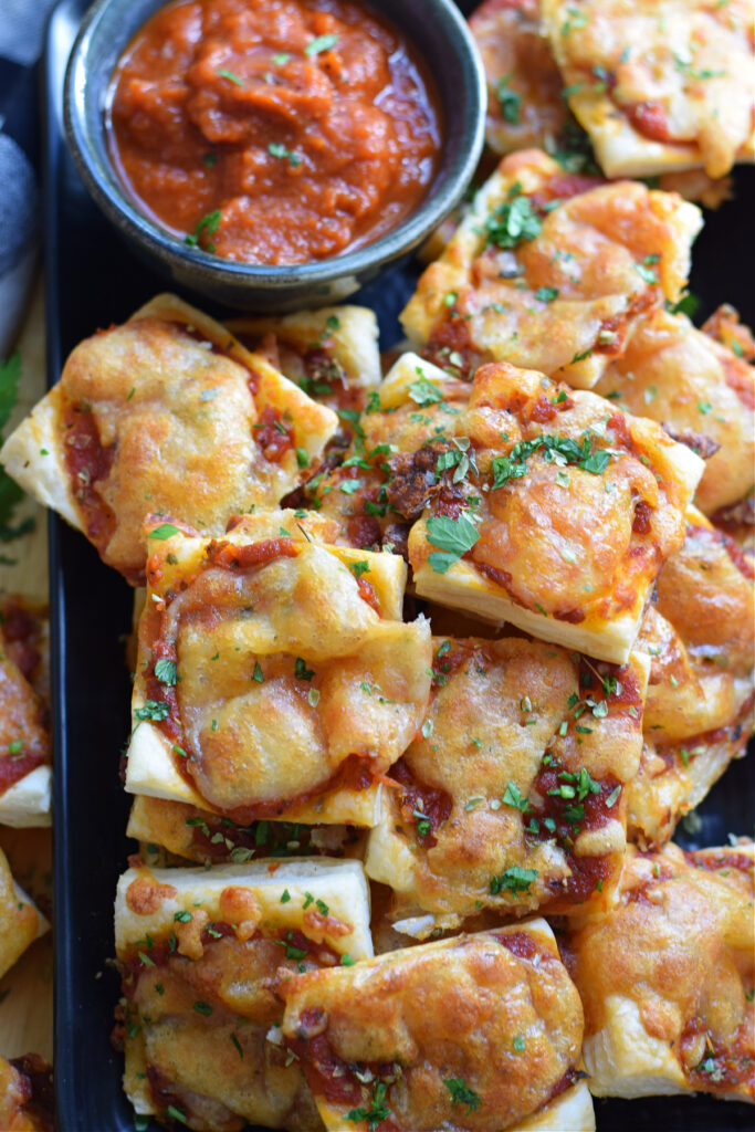 Puff pastry pizza bites on a plate with pizza sauce.