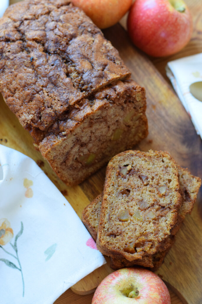 Apple cinnamon loaf cake on a board with apples.