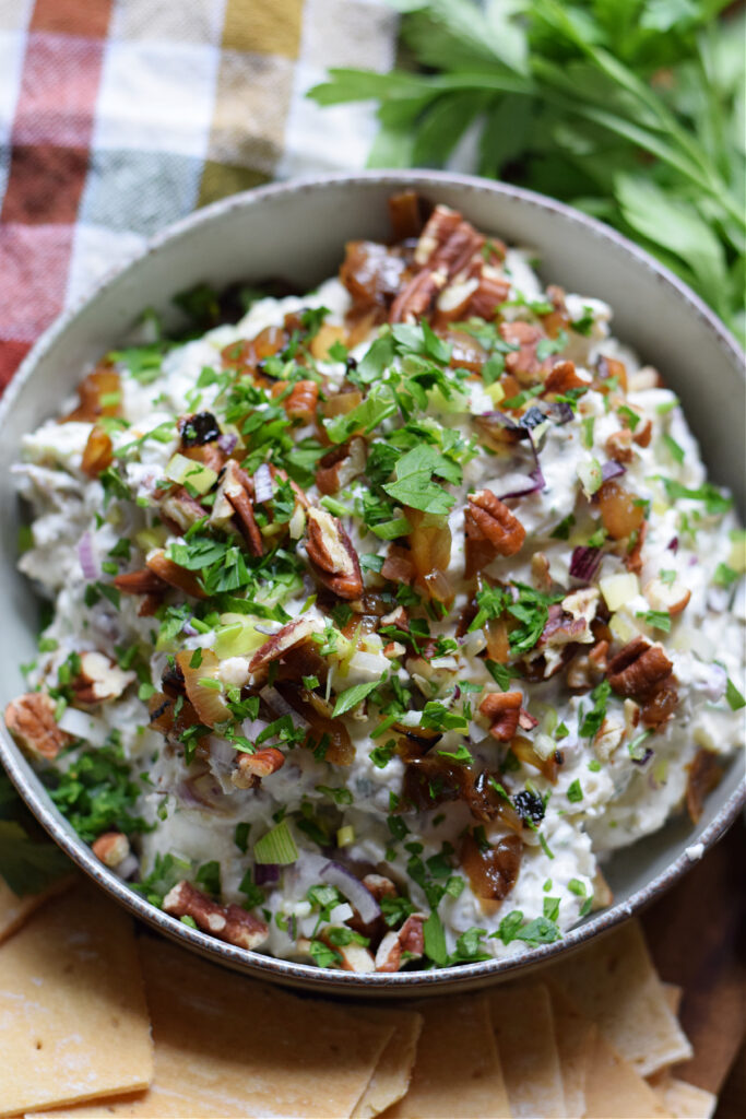Make this ultra rich and creamy Goat Cheese and Caramelized Onion Dip this holiday season.  A creamy goat cheese dip filled with sweet caramelized onions, chopped pecans, sharp spring onions and herbs & spices.  Great served with your favourite fancy crackers!Goat cheese pecan dip in a serving bowl.
