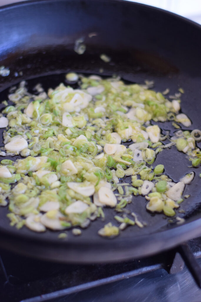 Cooking spring onions and garlic in a skillet.