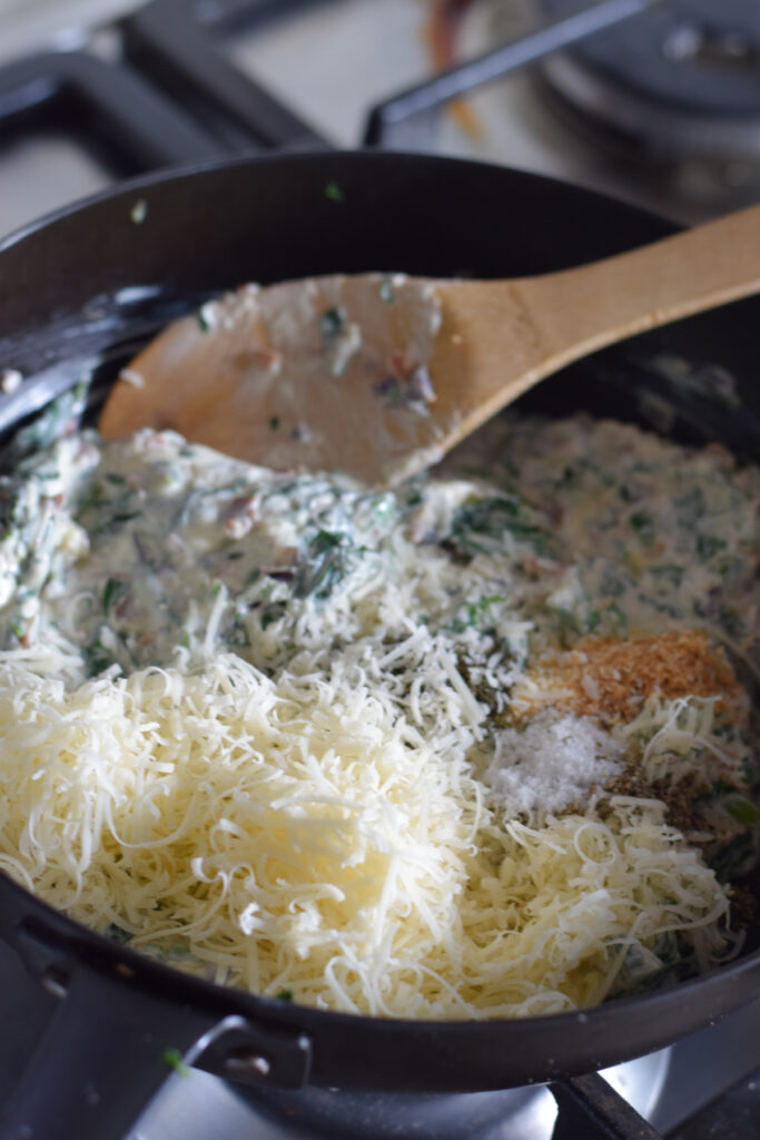 Adding parmesan cheese to a creamy filling in a skillet.