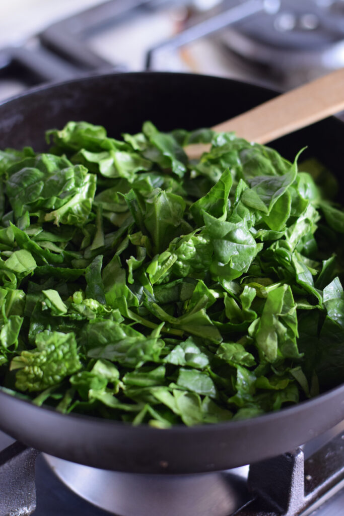 Adding spinach to a skillet.