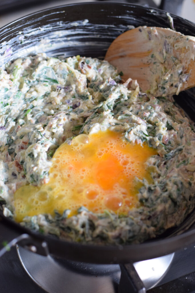 Adding egg to a creamy spinach filling.