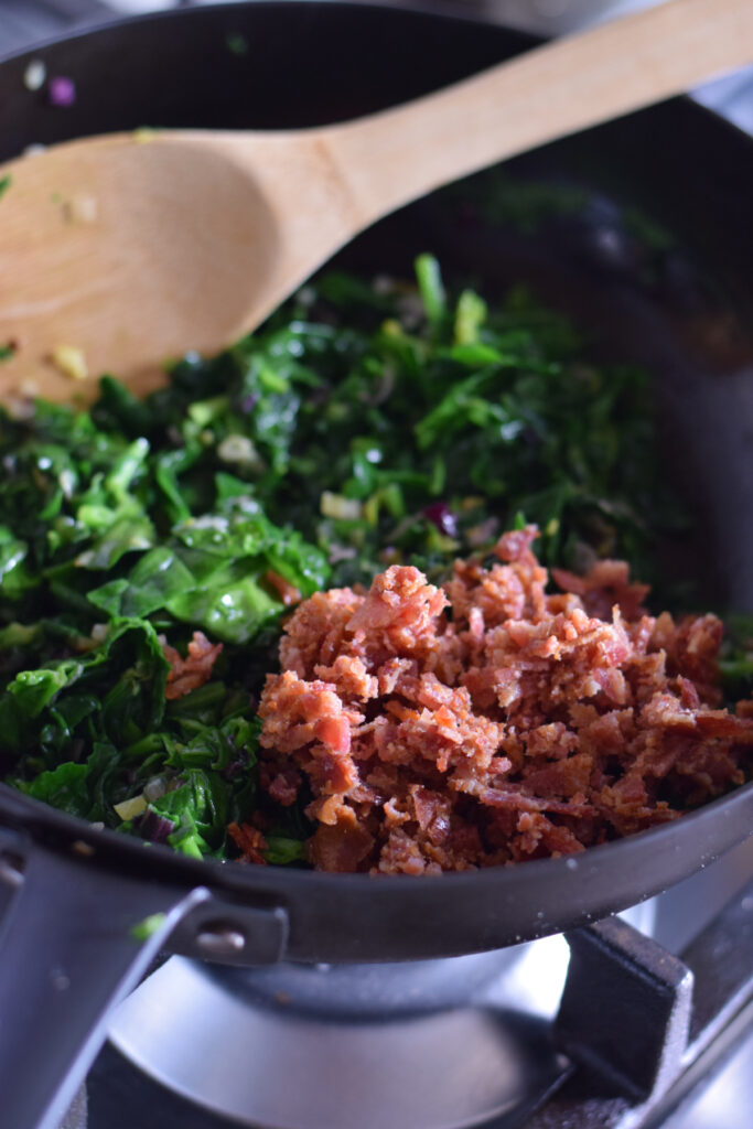 Adding bacon to spinach in a skillet.