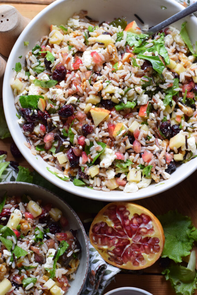 Wild rice salad in a bowl and with a pomegranate on the side.