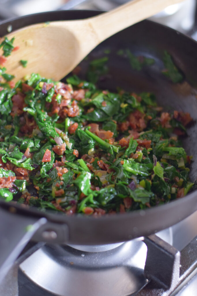 Cooking bacon and spinach in a skillet.