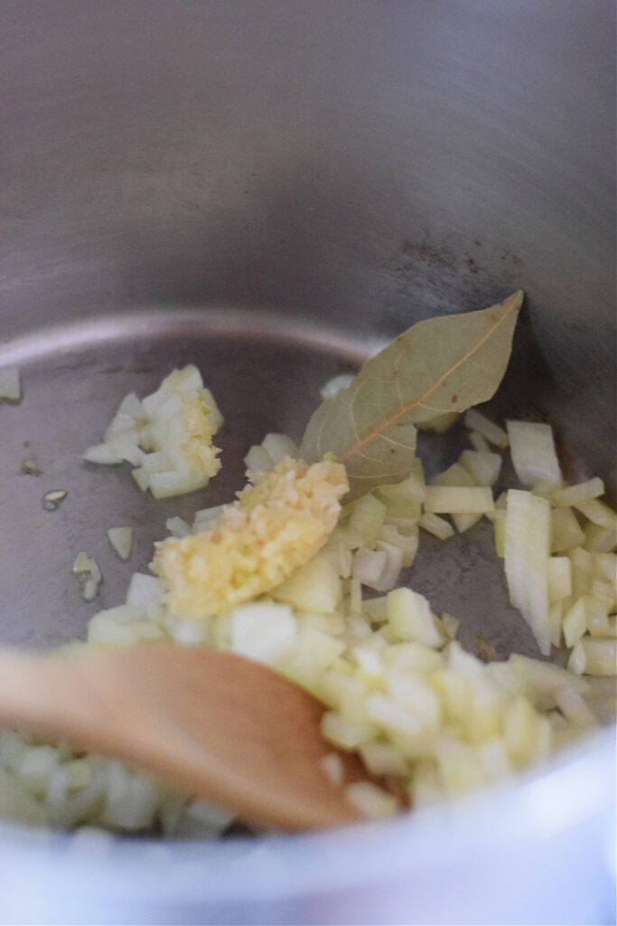 Cooking bay leaf and garlic with onions in a pot.