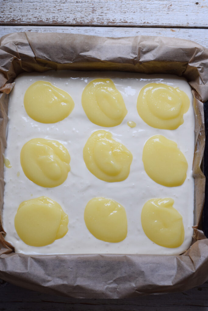 Adding lemon curd to cheesecake bars.