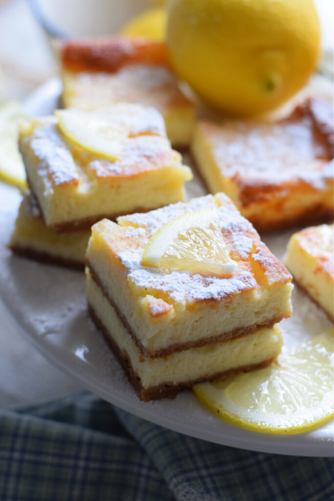 Lemon cheesecake bars on a plate with lemons.