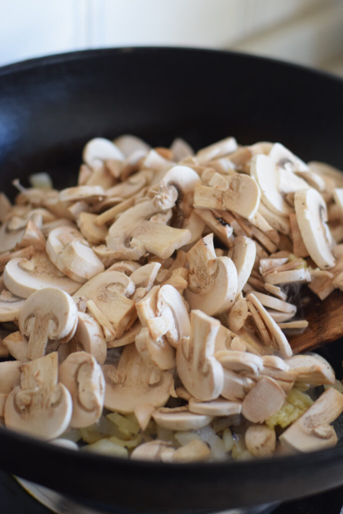 Adding mushrooms to a skillet.