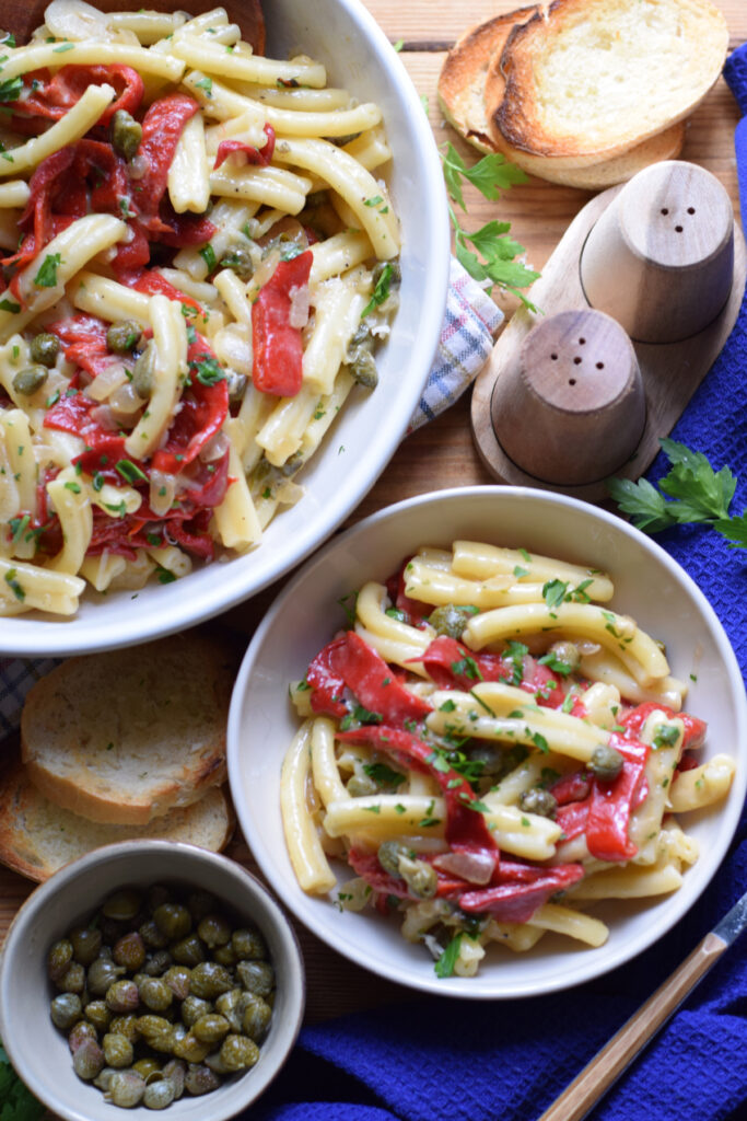 Pasta in bowls with red peppers and capers.