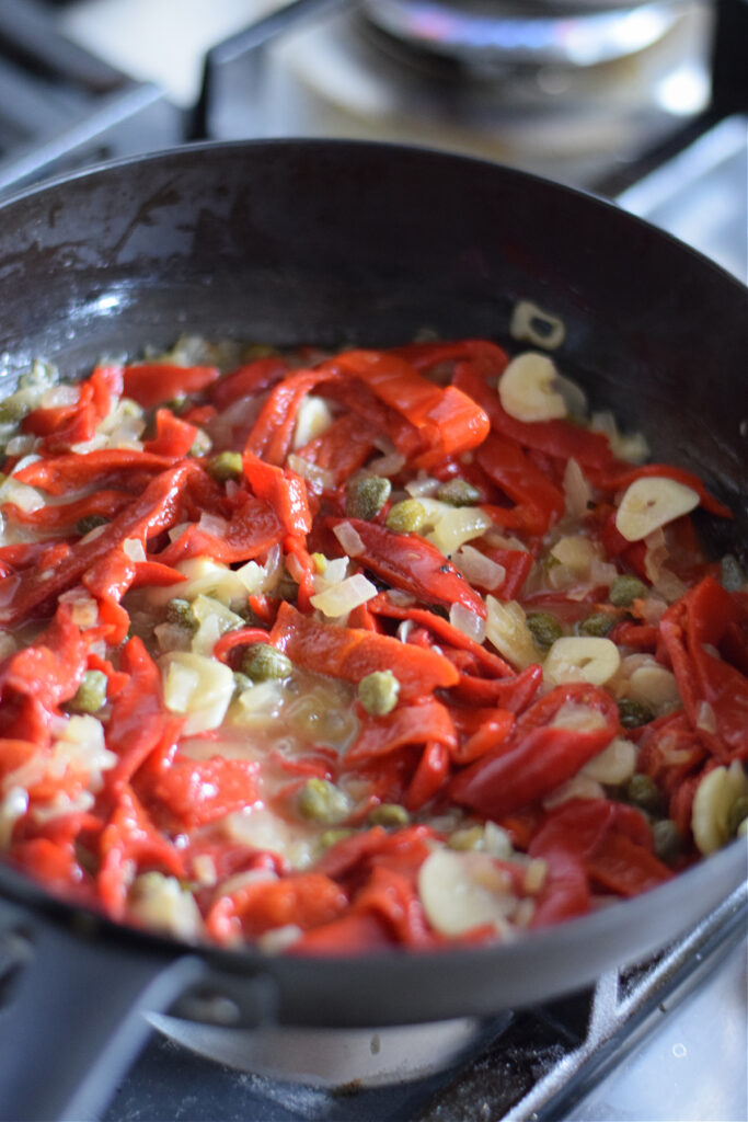 Cooking roasted red peppers with garlic and capers.