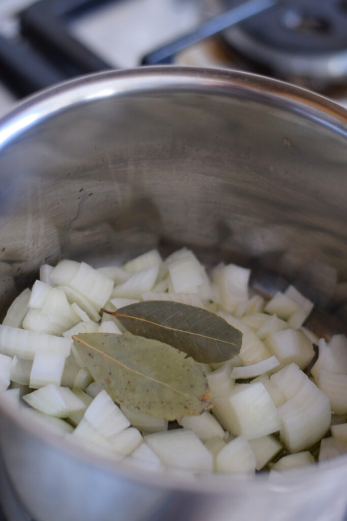 Adding garlic and bay leaves to onions in a pot.