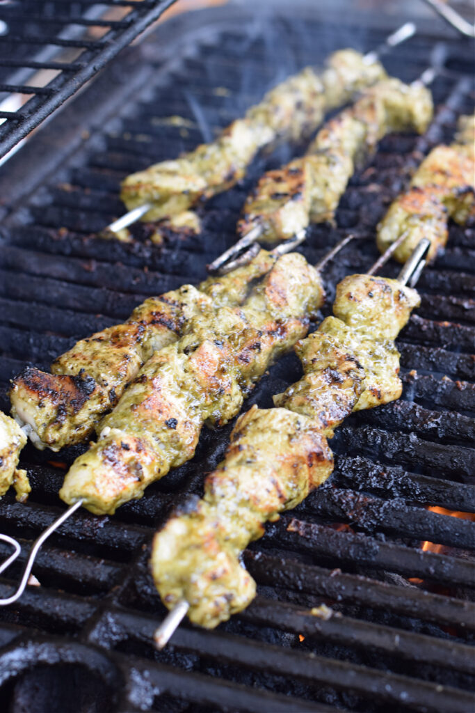 Cooking green pesto chicken kebabs on a barbeuce.