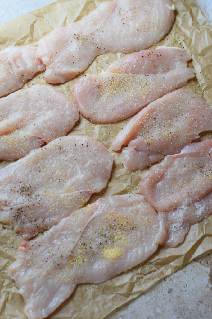 Seasoned chicken fillets on parchment paper.