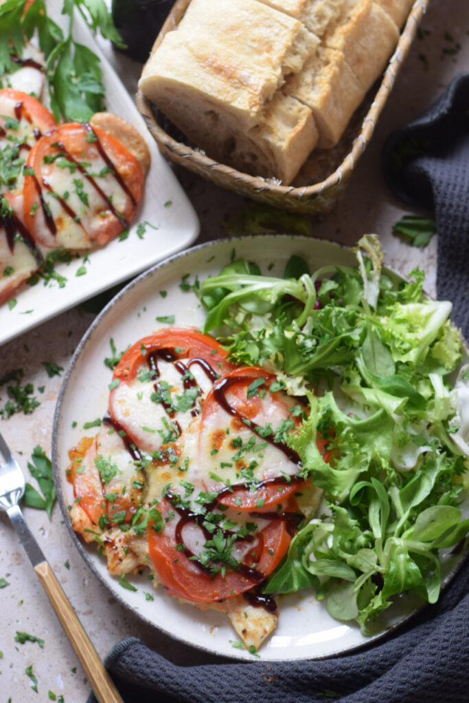 Mozzarella tomato topped chicken with salad on a plate.