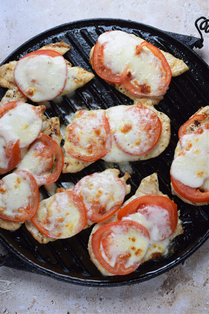 Tomato and mozzarella topped chicken in a skillet.