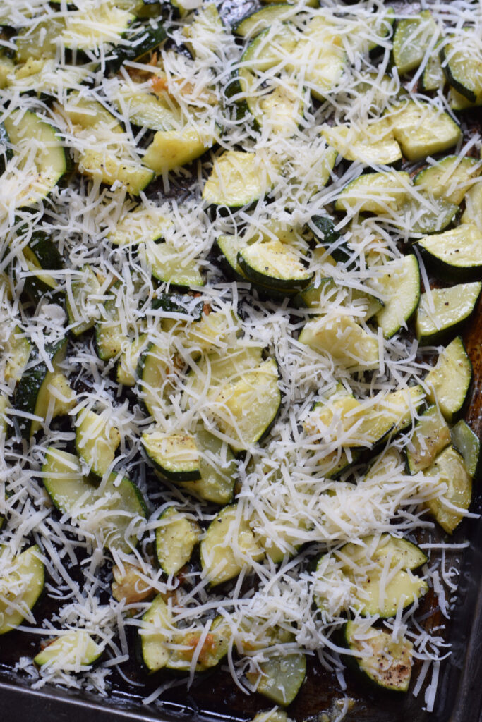Zucchini topped with parmesan cheese on a baking tray.