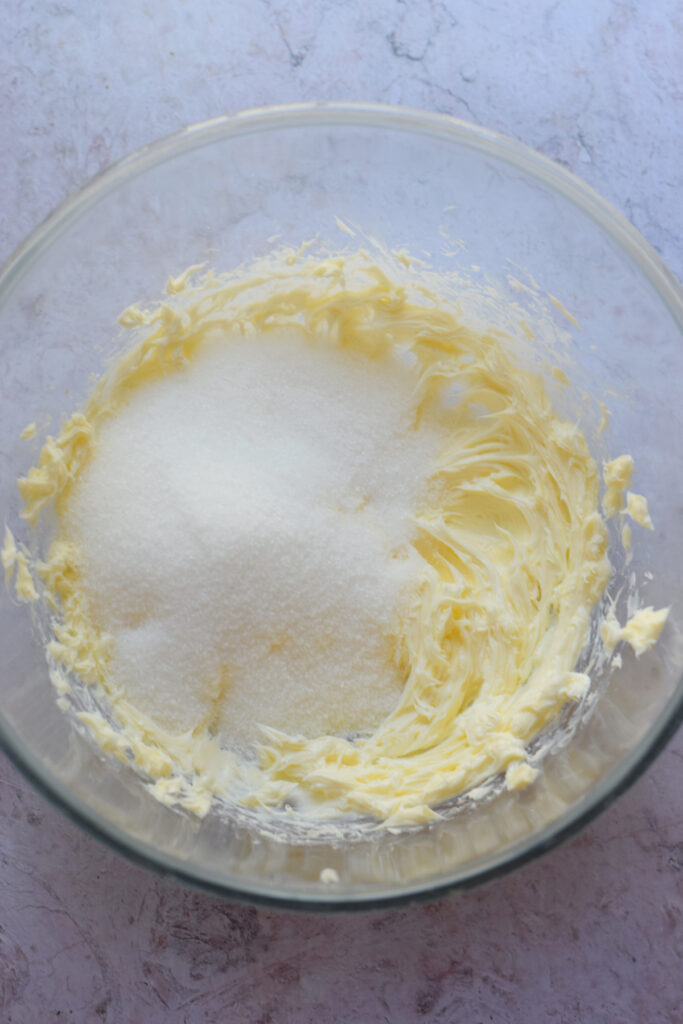 Adding sugar to butter in a mixing bowl.