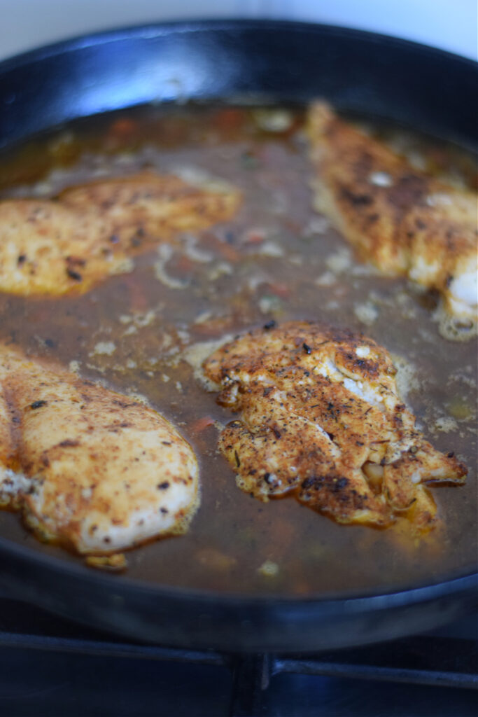 Cooking chicken in a skillet with broth and rice.